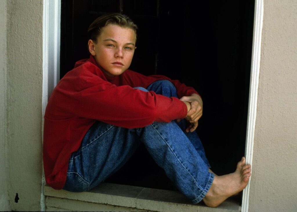 Leonardo DiCaprio kao dete sedi na prozoru u crvenom d\emperu i jeans farmerkama